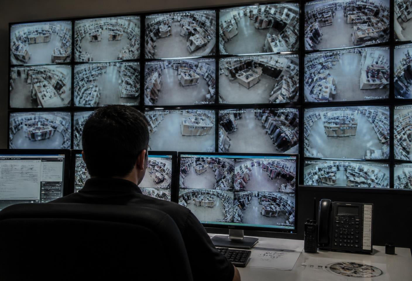 Security operator watching a wall of CCTV monitors showing store feeds