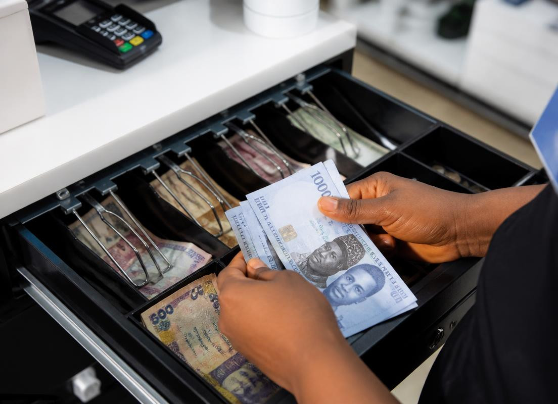Hands counting naira notes at an open cash drawer